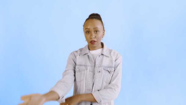 Портрет расстроенной африканской девушки-американки с недоумением смотрит в камеру на синем фоне. Лицо ладони Жана куртка — стоковое видео