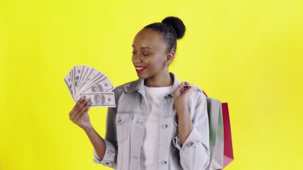 Retrato de mulher afro-americana com sacos de compras e fã de dinheiro no fundo amarelo no Studio. Casaco Jean — Vídeo de Stock