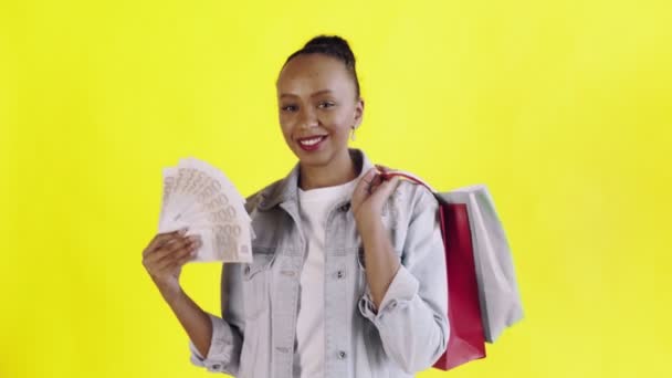 Retrato de mujer afroamericana con bolsas de compras y abanico de dinero sobre fondo amarillo en Studio. Chaqueta Jean — Vídeos de Stock