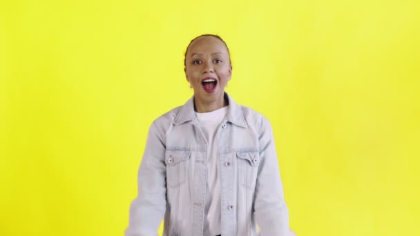 Hermosa joven africana feliz sorprendida mientras mira a la cámara y dice OH MI DIOS sobre fondo amarillo chaqueta Jean — Vídeo de stock