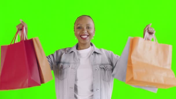 Portrét afroamerické ženy s nákupními taškami na zeleném pozadí ve studiu. Šťastná žena drží nákupní barevné tašky. Jean bunda — Stock video
