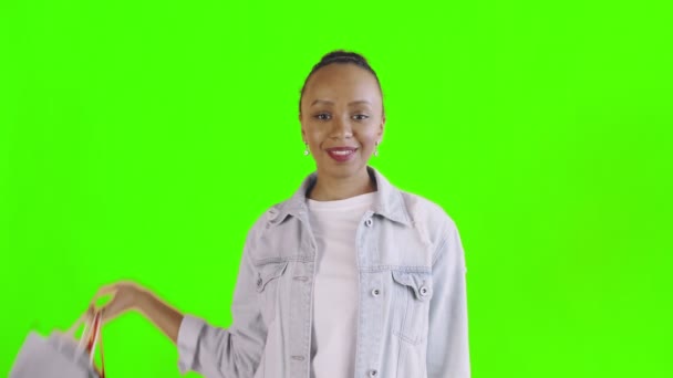 Retrato de mulher afro-americana com sacos de compras está mostrando polegares para cima no fundo verde no estúdio. Casaco Jean — Vídeo de Stock