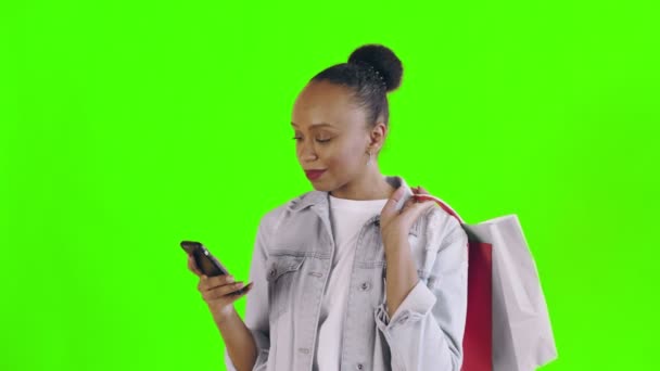 Portrét africké Američanky s nákupními taškami mluví smartphonem na zeleném pozadí ve studiu. Jean bunda — Stock video