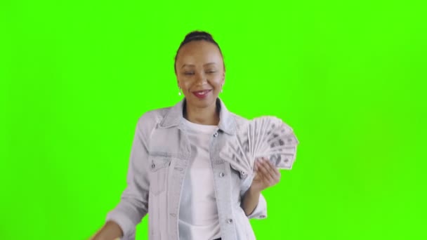 Elégedett boldog izgatott afro-amerikai nő bemutató pénz és tánc a kamera zöld háttér Jean kabát — Stock videók
