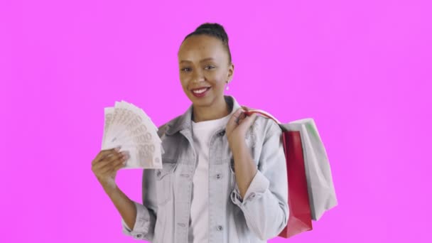 Retrato de mujer afroamericana con bolsas de compras y abanico de dinero en rosa Fondo en Studio. Chaqueta Jean — Vídeos de Stock