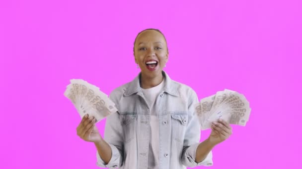 Tevreden gelukkig opgewonden Afrikaans amerikaanse vrouw tonen geld en zeggen O mijn god op roze achtergrond Jean jas — Stockvideo