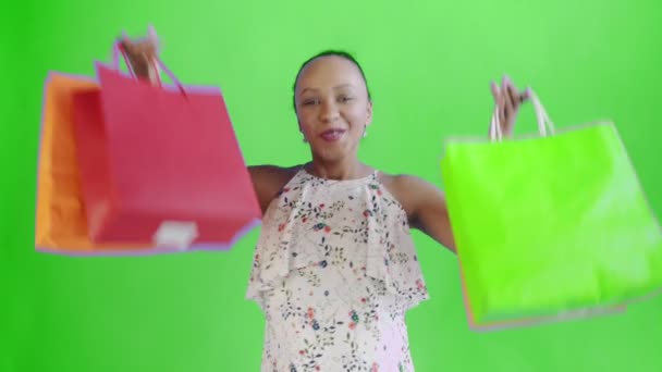 Retrato de mujer afroamericana bailando con bolsas de compras sobre fondo verde en Studio. Mujer feliz sosteniendo compras coloridas bolsas. Vestido blanco con flores — Vídeo de stock