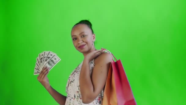 Afrikai amerikai nő, pénzes kártyával és bevásárlószatyrokkal. Zöld vászon. Fehér ruha virágokkal — Stock videók
