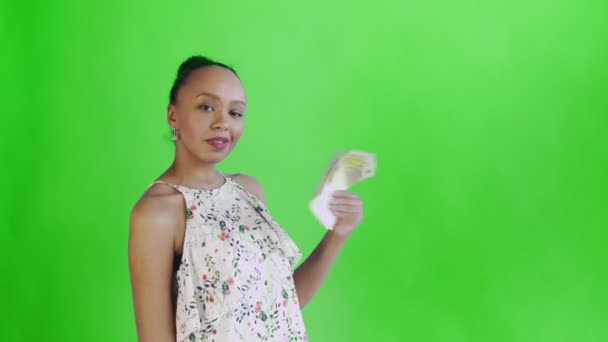Αφροαμερικανή γυναίκα με χρήματα ανεμιστήρα δείχνει τον αντίχειρα επάνω στο πράσινο φόντο στο στούντιο. Λευκό φόρεμα με λουλούδια — Αρχείο Βίντεο