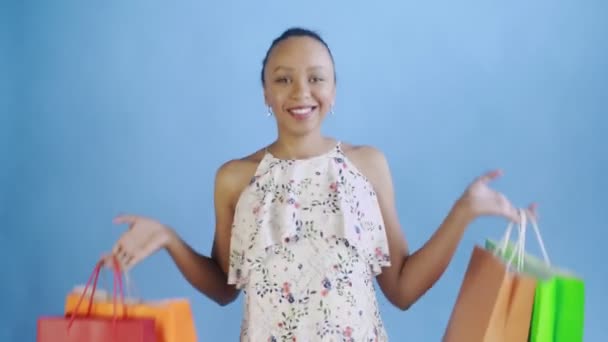 Retrato de mulher afro-americana está dançando com sacos de compras em fundo azul no Studio. Happy Woman Holding Sacos coloridos de compras. Vestido branco com flores — Vídeo de Stock