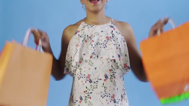 Зв'язок афро-американської жінки танцює з торбами на синьому фоні в студії. Щаслива жінка, яка краде барвисті мішки. Біла сукня з квітами. — стокове відео
