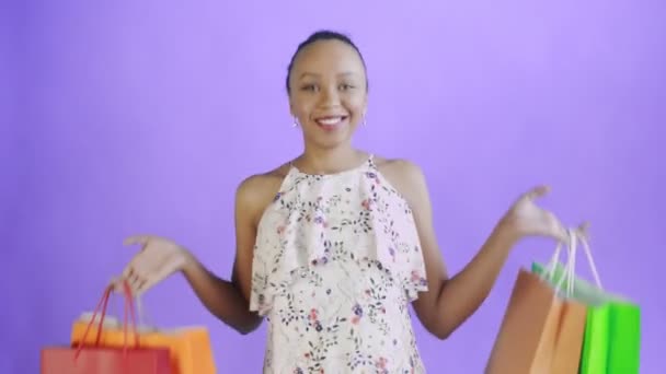 Retrato de mujer afroamericana bailando con bolsas de compras sobre fondo púrpura en Studio. Mujer feliz sosteniendo compras coloridas bolsas. Vestido blanco con flores — Vídeo de stock