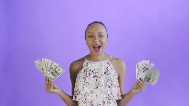 Zadowolony szczęśliwy podekscytowany Afryki amerykańskiej kobieta pokazując pieniądze i mówiąc O Mój Boże na fioletowym tle Biała sukienka z kwiatami — Wideo stockowe