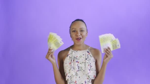 Spokojen šťastný nadšená africká americká žena ukazuje peníze a říká Ó můj Bože na fialovém pozadí. Bílé šaty s květinami — Stock video