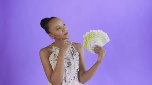 Pensativa mujer afroamericana exitosa con dinero sobre fondo púrpura. Vestido blanco con flores — Vídeos de Stock