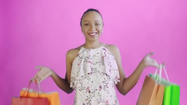 Porträt einer afrikanisch-amerikanischen Frau tanzt mit Einkaufstaschen auf rosa Hintergrund im Studio. glückliche Frau mit bunten Einkaufstaschen. weißes Kleid mit Blumen — Stockvideo