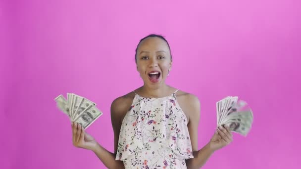 Satisfied happy excited african american woman showing money and saying O MY GOD on pink background White dress with flowers — Stockvideo