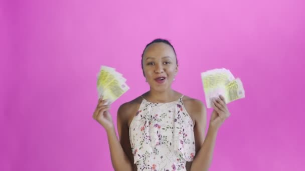 Satisfied happy excited african american woman showing money and saying O MY GOD on pink background. White dress with flowers — 图库视频影像