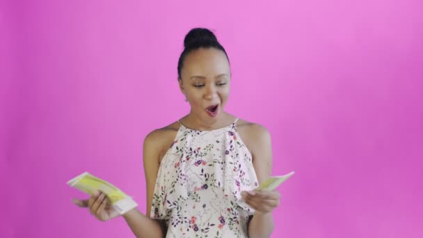 Attractive Afro american woman is counting money against a pink background. White dress with flowers — ストック動画