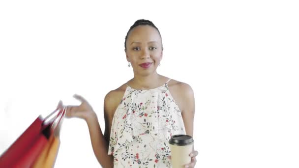 Retrato de una mujer afroamericana con bolsas de compras está bebiendo un café sobre fondo blanco en Studio. Vestido JWhite con flores — Vídeos de Stock