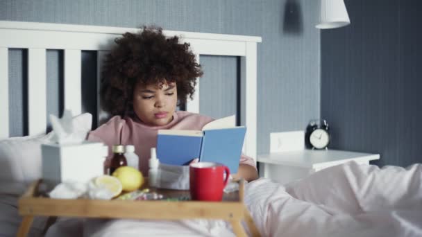 Una mujer tiene un resfriado en casa. Acostado en la cama con un libro . — Vídeo de stock