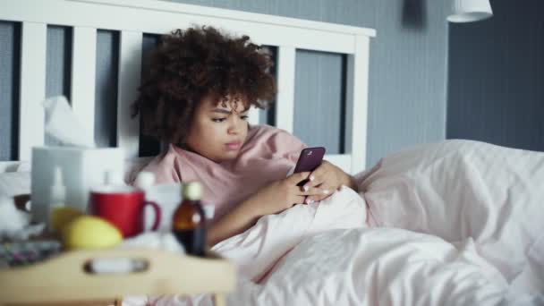 Enfermo joven afroamericano chica usando el teléfono en la cama en casa — Vídeos de Stock