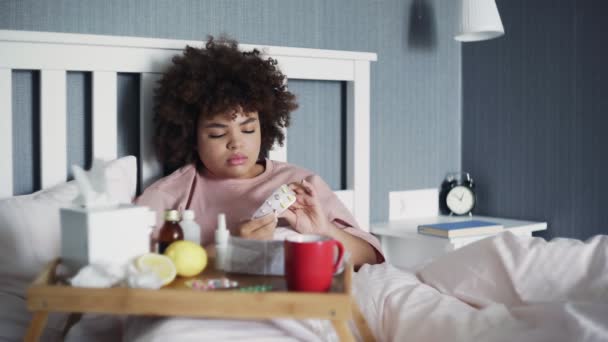 病気のアフリカ系アメリカ人の女の子は、自宅でベッドに横たわって、水で丸薬を取ります — ストック動画