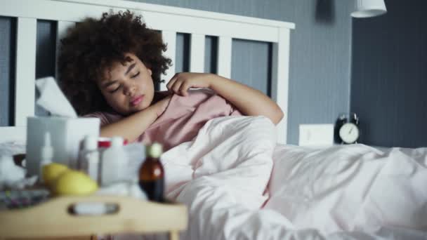 生病的非洲裔美国女孩感冒躺在家里的床上。体温计检查温度的年轻黑人妇女 — 图库视频影像
