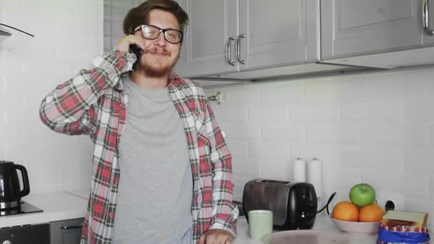 Mladý muž si bere plátek chleba z toustovače, aby dělal sendviče, zatímco mluví po telefonu — Stock video