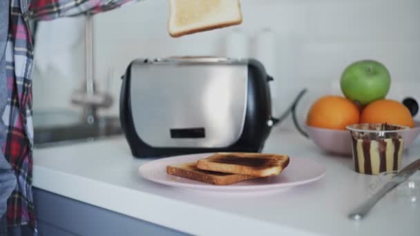Молодой человек берет ломтики хлеба из тостера, чтобы сделать бутерброды — стоковое видео
