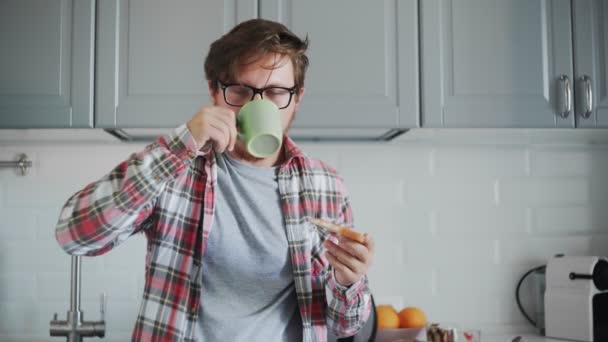 Young man eating toast with strawberry jam and drinking coffee or tea — Stock Video