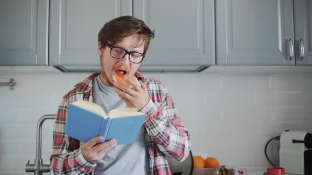 Ung man äter rostat bröd med jordgubbssylt och läser en bok — Stockvideo