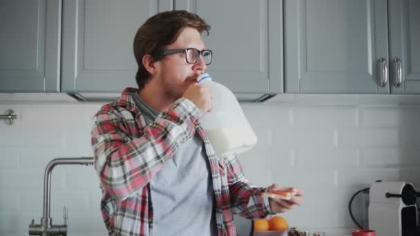Молодой человек ест тосты с клубничным джемом и пьет молоко из пластиковой бутылки — стоковое видео