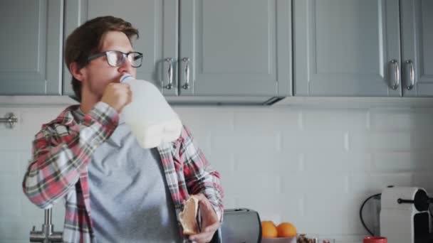 Young man eating toast with chocolate paste and drinking a milk from plastic bottle — Stock Video