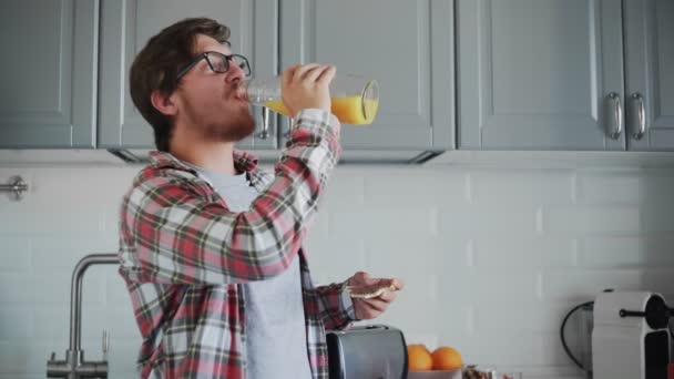 Mladý muž jí toast s čokoládovou pomazánkou a pije pomerančovou šťávu — Stock video