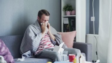 Oturma odasında kanepede oturan bir adam burnunu siliyor.