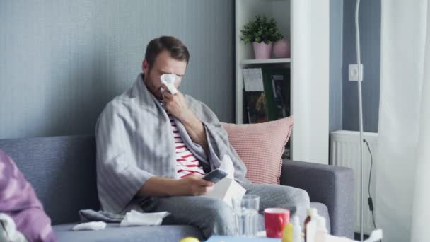 Sick man with flu at home, ill young man with fever watching tv show and using remote control. — Stock Video