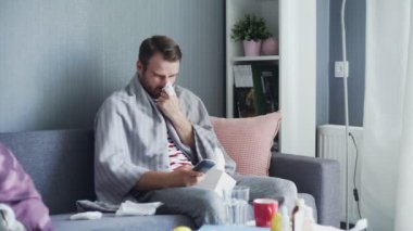 Evde grip olmuş hasta bir adam, ateşi olan bir genç adam televizyon seyrediyor ve uzaktan kumanda kullanıyor..