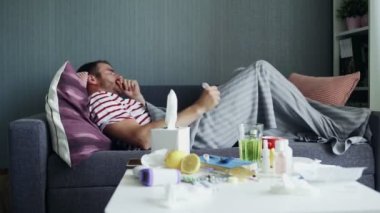 Hasta genç bir adam bir hastalık sırasında uyumaya çalışır, sıcak bir battaniyenin altındaki bir dairede kanepede yatar..