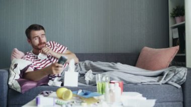 Evde grip olmuş hasta bir adam, ateşi olan bir genç adam televizyon seyrediyor ve uzaktan kumanda kullanıyor..