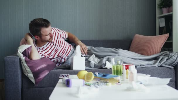 A sick young man tries to fall asleep during an illness, lying on a sofa in an apartment under a warm blanket. — Stock Video