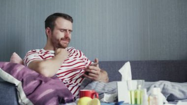 Hasta genç adam telefon kullanıyor ve burnunu mendille siliyor.