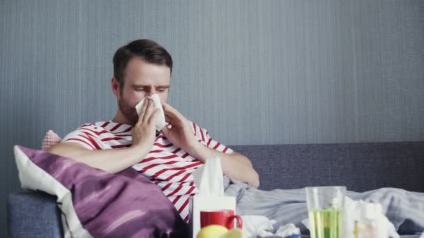 Een man hoest zwaar, snuit zijn neus terwijl hij op een bank in de woonkamer zit — Stockvideo