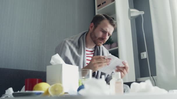 Een volwassen zieke man zit op de bank en neemt voorgeschreven medicatie voor ziekte. — Stockvideo