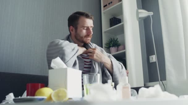 Nemocný muž s chřipkou sedí doma na gauči. Nemocný mladý muž se studenou kontrolní teplotou s teploměrem — Stock video
