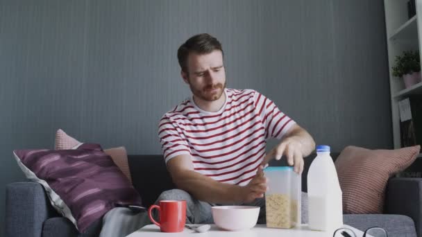 Barbudo hombre vierte copos de corcho en una taza para preparar el desayuno — Vídeos de Stock