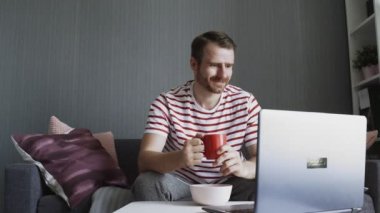 Sakallı, gülümseyen adam çay içiyor ve bilgisayarı kaydırıyor..