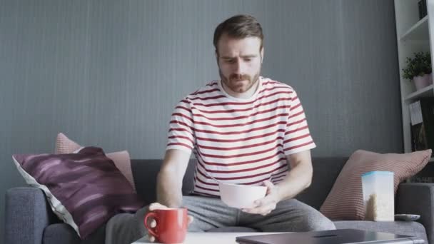 Sakallı adam kahvaltı yapıyor ve dizüstü bilgisayar kullanıyor. — Stok video