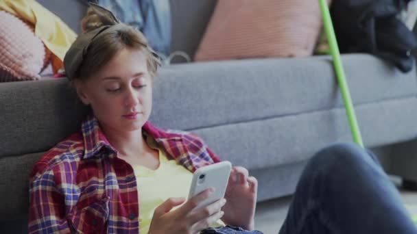 Молодая женщина лежит на полу после уборки и пользуется телефоном — стоковое видео
