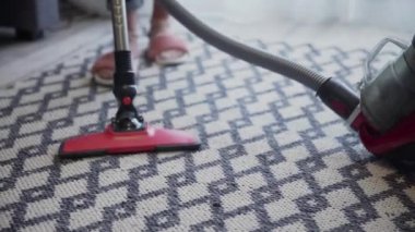 Halıyı temizlemek için elektrikli süpürge kullanan genç bir kadın.